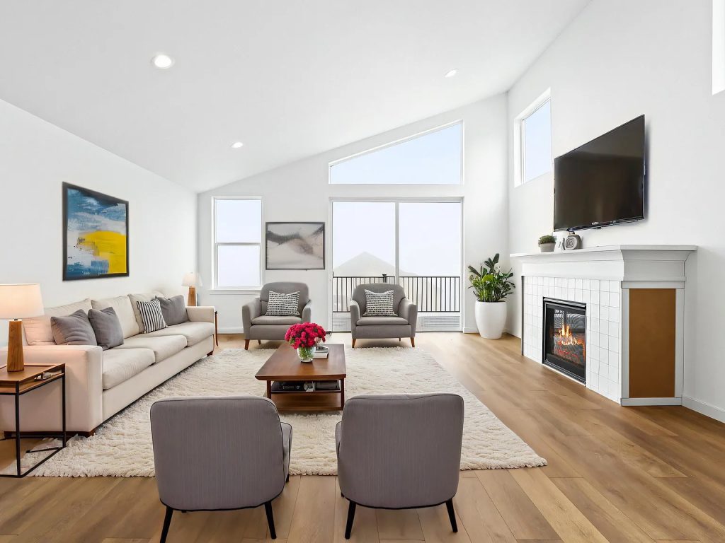 Living room with vaulted ceiling, tall windows, and a tiled fireplace